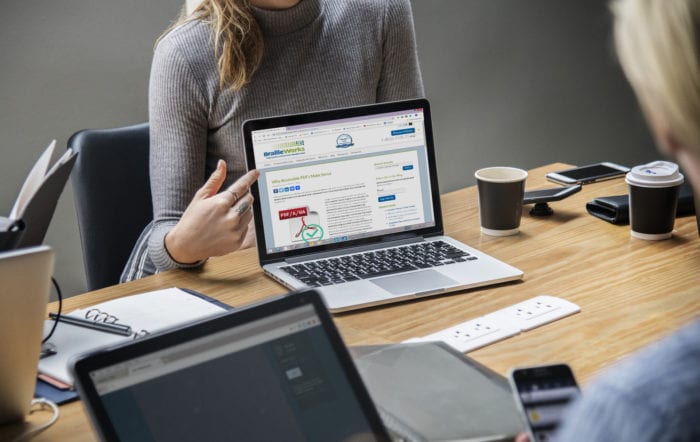 Work meeting with a woman pointing to a laptop screen with Braille Works blog "Why Accessible PDFs Make Sense"