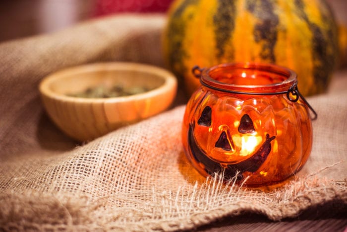 Jack-o-lantern holding a lit candle, bowl, and gourd on burlap