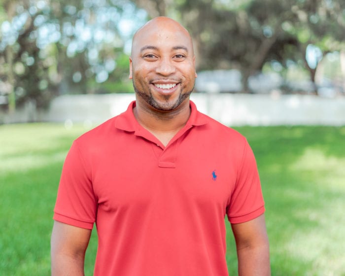 Larry Layton smiling and standing in a grassy field with a fence and oak trees in the background