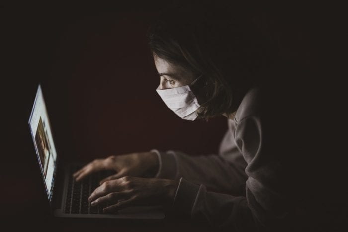 Someone with a mask close up to their computer screen reading COVID 19 communication.