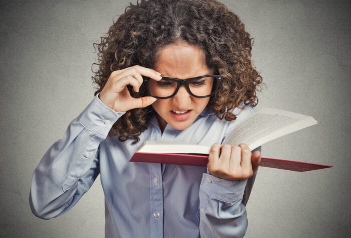 Woman with glasses struggling to read the print in a book