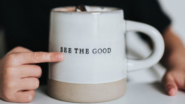 Finger pointing to a mug that says "See the good"