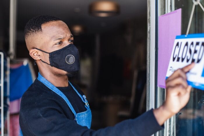 Man wearing mask turns sign to "closed"