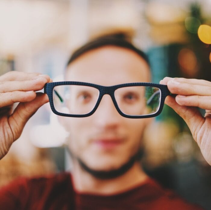 Blurry image of a man holding up in-focus glasses