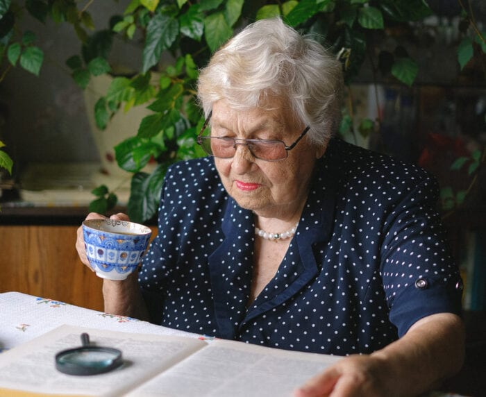 Senior citizen woman reading a book while drinking tea