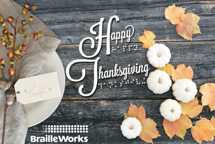 The words Happy Thanksgiving in print and braille surrounded by small pumpkins, autumn leaves, and a decorated plate with the Braille Works logo