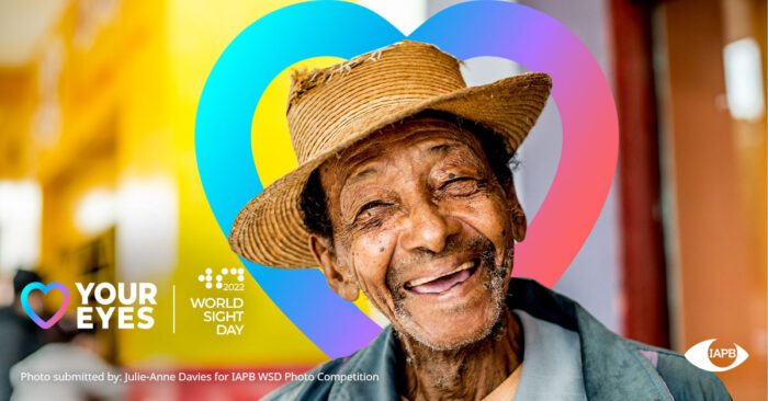 Man wearing a straw hat who's smiling and squinting in the sun. There's a heart behind his head and along with various World Sight Day partner logos
