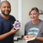 Two Braille Works employees smiling while holding up donuts on National Donut Day.