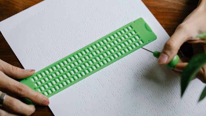 Hands using a slate and stylus to braille paper