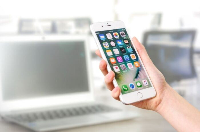 A person holding up a phone in front of a computer.
