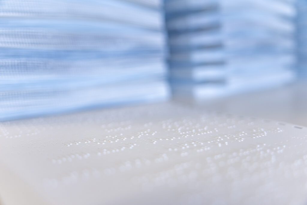 Close up on embossed paper with stacks on braille paper in the background