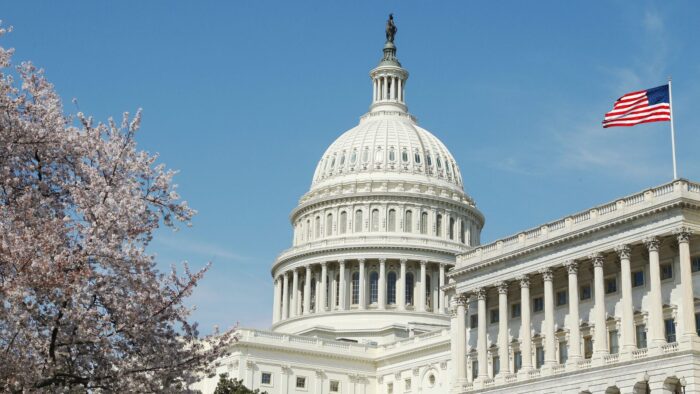 U.S. Capitol building with an American flag waving against a clear blue sky